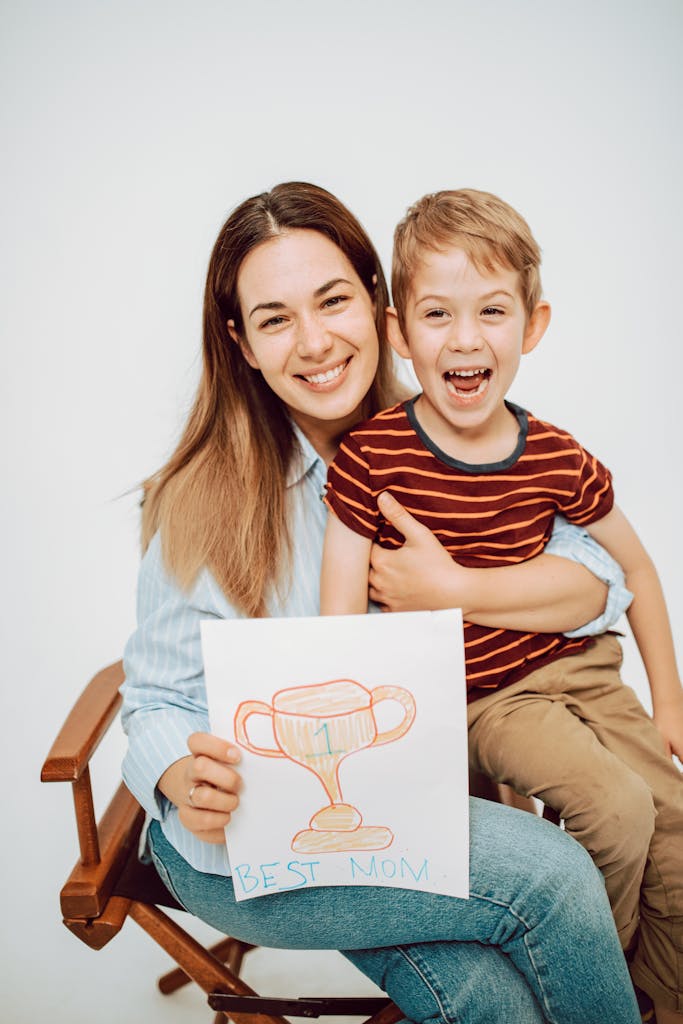 Mother and son smiling together holding a 'Best Mom' drawing of a trophy.
